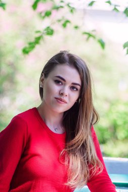 Kırmızı ceket. Kız parkta yürüyor. Bankta oturur.