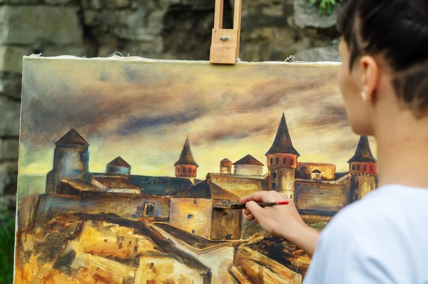 Student artist paints painting paint and brush. The picture depicts an old fortress in the city of Kamyanets-Podilsky. Very old castle.