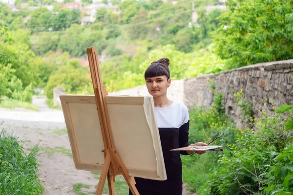 Student artist paints painting paint and brush. The picture depicts an old fortress in the city of Kamyanets-Podilsky. serious art