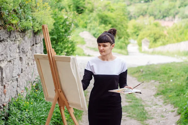 Student artist paints painting paint and brush. The picture depicts an old fortress in the city of Kamyanets-Podilsky. serious art