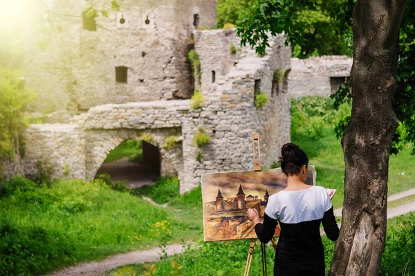 Student artist paints painting paint and brush. The picture depicts an old fortress in the city of Kamyanets-Podilsky.