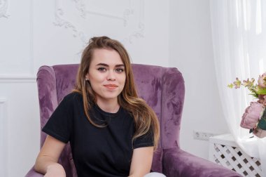 Kız koltukta oturuyor. Mor renk... Beyaz Siyah T-shirt pantolon. Stüdyo vurdu.