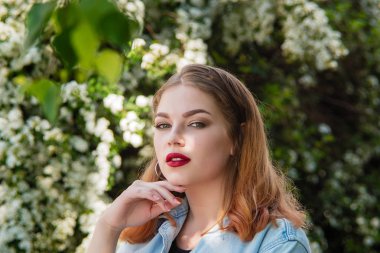 Beyaz çiçeklerin arka planında parkta kot ceketli bir kız..