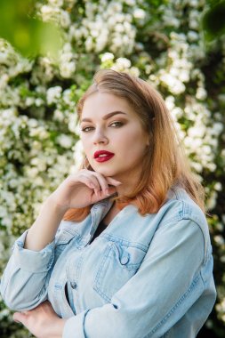 Beyaz çiçeklerin arka planında parkta kot ceketli bir kız..