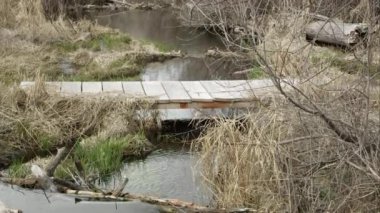 Kış sonrası manzara ile dere üzerinde küçük köprü görünümü.