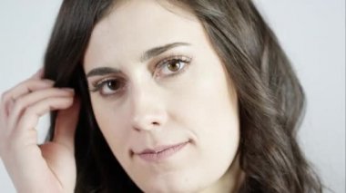 Saçlarını elleriyle tarayan ve stüdyoda beyaz perdeye gülümseyen genç bir kadın..