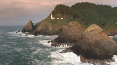 Oregon'da gün batımı sırasında Heceta Head Deniz Feneri'nin altındaki kayalara çarpan dalgaların havadan görünümü.