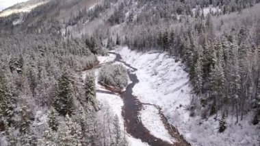 Utah dağlarının ormanında karla kaplı arazide akan nehrin üzerinde uçan havadan manzara.