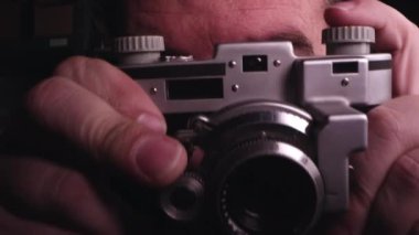 Karanlık odada deklanşör tuşuna basarak odak ayarlama vizör aracılığıyla bakmak için vintage fotoğraf makinesi yükselterek adam.