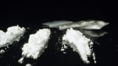 Up close macro view over lines of cocaine on black table moving over the white powdered drug viewing razor and baggie.