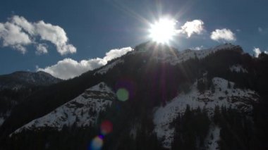 Dağ manzarasında geriye doğru uçarken Güneş ve dağ tepelerinin görünümü.