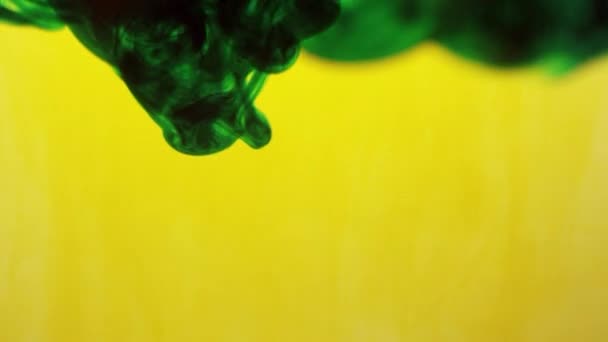 Encre verte et encre jaune se mélangeant dans l'eau tourbillonnant tandis que le jaune s'estompe .