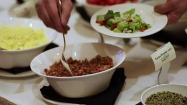 Salata barında salataya pastırma parçaları serpiştiren kişi.