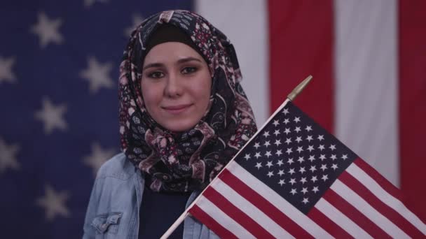 イラクからの遺産の一部としてヘッドスカーフを身に着けているアメリカ国旗を持って誇らしげに微笑むアメリカの女性 — ストック動画
