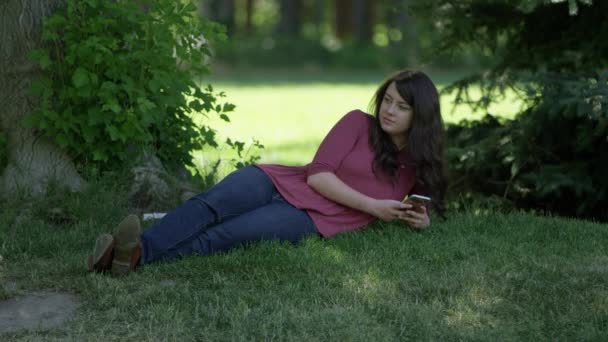 Jonge Vrouw Liggend Het Gras Looing Haar Telefoon Een Park — Stockvideo