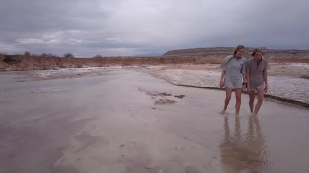 犹他州多云的一天 两名年轻女子在沙漠河上游徒步 — 图库视频影像