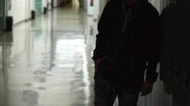 O okulda karanlık ve boş koridorda oturur gibi müzik dinleme onun dolap yalnız ayakta genç.