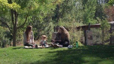 Otların arasında oturup bir parkta piknik yaparken yemek yiyip içen aile.