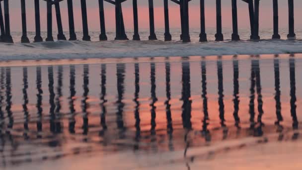 ニューポートビーチの夕日のビーチで桟橋を通して空に色を反射する水 — ストック動画