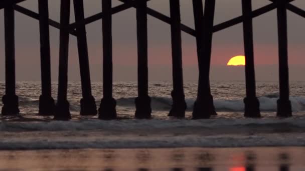 太陽が雲の後ろに行くように海の波を見る桟橋の後ろに沈む太陽 — ストック動画