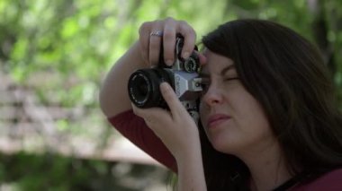 Vizörün içinden bakarken film kamerasını dikey tutan genç kadın ve fotoğraf çekmek için odağı ayarlar.