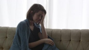 Onu yüzüne elini tutarak battaniye sarılmış kanepede oturan stresli kadın.