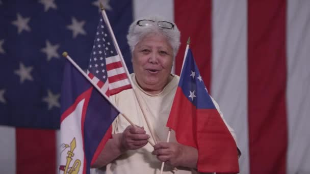 悬挂萨摩亚国旗 美属萨摩亚国旗和美国国旗的妇女站在美国国旗前 — 图库视频影像