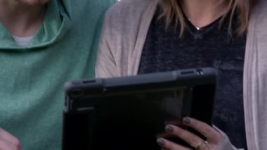 Genç beyaz çift büyük ağacın altında ipad kullanıyor.