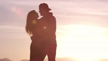 Birbirine aşık genç bir çift gün batımında dağlarda dinleniyor.