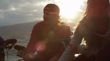 Açık havada yanan ateşin yanında dinlenen bir grup genç