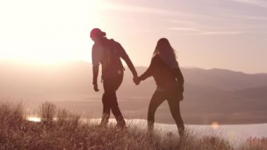 Birbirine aşık genç bir çift gün batımında dağlarda dinleniyor.