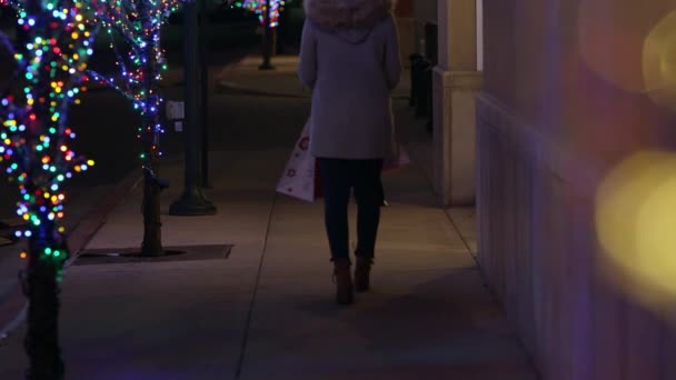 女性はクリスマスの夜に路上で買い物袋を持って歩いています — ストック動画