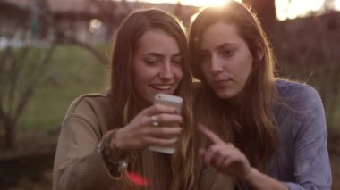 İki ikiz kız kardeş açık havada cep telefonu kullanıyor