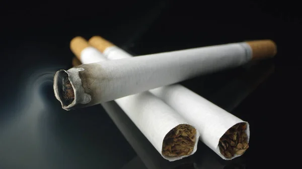 Dumanlar havada süzülürken siyah masanın üstünde yanan sigaranın görüntüsü.