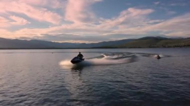 Rengarenk günbatımında, bir su aracını takip eden hava aracı, insanları iple çekiyor..