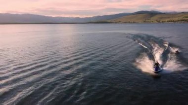Bir su aracı, sörf tahtasındaki kişiyi eğlence için keskin bir dönüş yaptıktan sonra gölün karşısına fırlatıyor..
