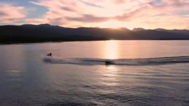 Gölün üzerinde renkli bir gün batımı. Suyun üzerinde hız kazanmak ve suyun üzerinde uçmak için insanları sörf tahtasına çeken bir tekneyi takip ediyor..