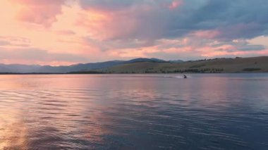 Bir su teknesi Hebgen Gölü 'nde oynarken gün batımında çekilen ve kırbaçlanan kişi sıkı bir dönüş yapar..