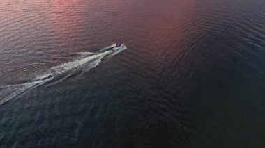 Gün batımı gölde yansıyor. Bir su aracının birini havadan çekişini seyrederken..