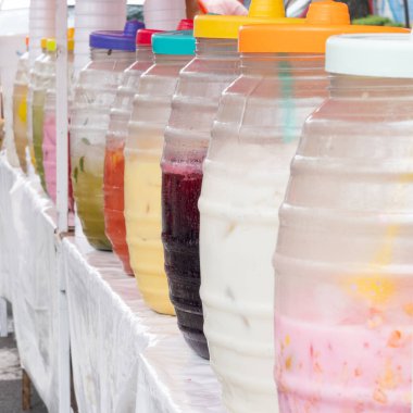 A row of pitchers of different colored drinks are lined up on a table. The drinks are in clear glass jars and are arranged in a row