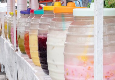 A row of pitchers of different colors and flavors are lined up on a table. The pitchers are filled with various drinks, including fruit punch, lemonade, and iced tea