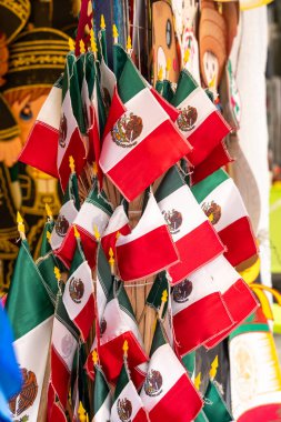 A display of Mexican flags with a variety of colors and designs. The flags are hanging on a wall or a pole