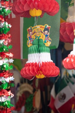 A bunch of paper lanterns hanging from the ceiling, one of which has a sticker that says 