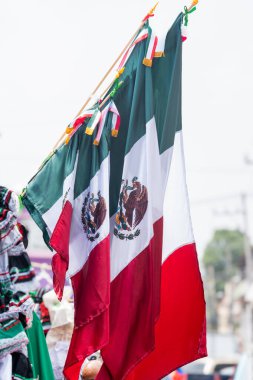 Three flags with the Mexican flag in the middle. The flags are hanging from a pole. The flags are red, white, and green