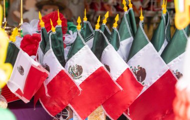 A display of Mexican flags with a red, white, and green design. The flags are arranged in a row and are hanging from a table