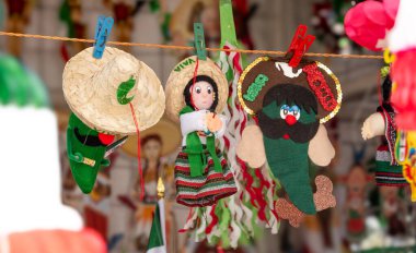 A collection of Mexican dolls hanging on a line. The dolls are wearing hats and clothing, and some of them have faces. Concept of cultural celebration and festivity