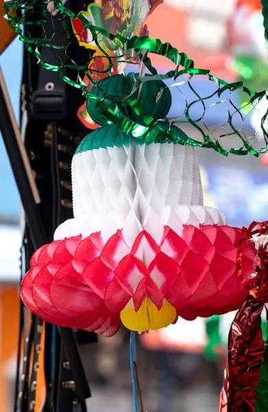 Yeşil saplı kırmızı beyaz kağıt bir çiçek. Çiçek bir ipte sallanıyor.