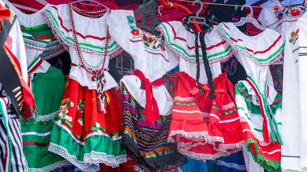 A rack of colorful dresses with a red and white dress in the middle. The dresses are from Mexico and are displayed for sale