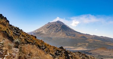 Gökyüzünde bulut olan bir dağ. Gökyüzü mavi ve dağ kahverengidir. Dağ çok yüksek ve bulutlar beyazdır. popocatepetl volkan Meksika,