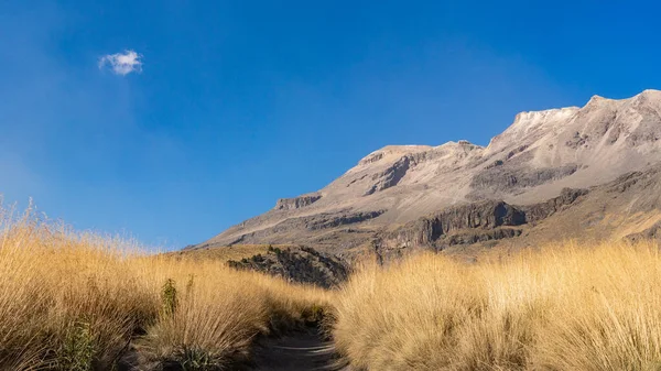 Uzakta açık mavi gökyüzü ile bir dağ sırası görülebilir. Dağlar çimlerle kaplı ve gökyüzü parlak ve güneşli. Iztacihuatl popocatepetl Yanardağ Meksika,